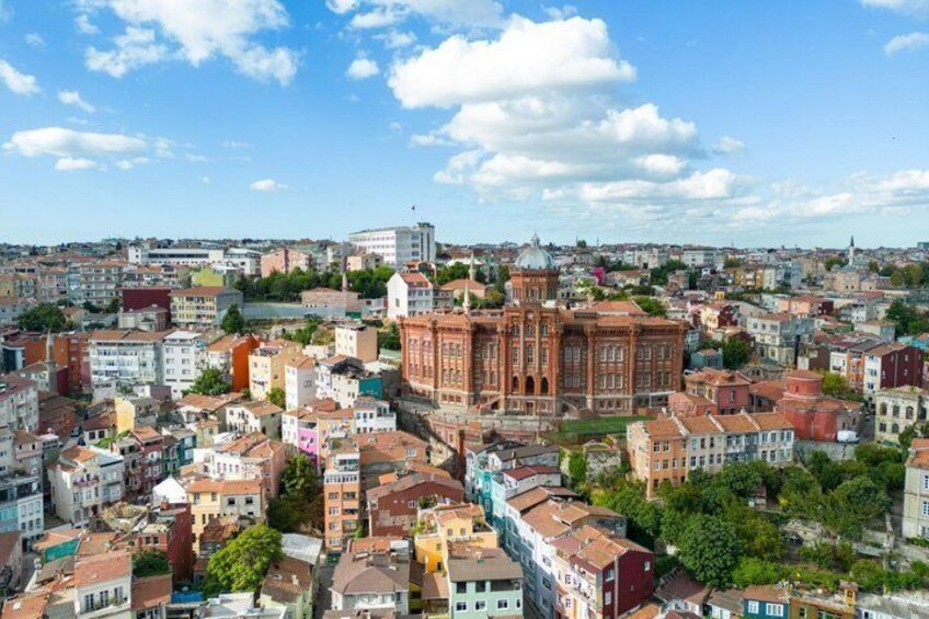 A cityscape with a prominent red-brick building, likely a historical or cultural landmark, surrounded by a mix of residential and commercial buildings. 5