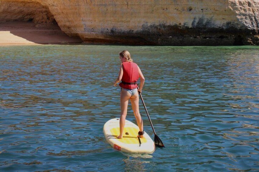 A person paddleboarding on clear water with a rocky shoreline in the background. 4