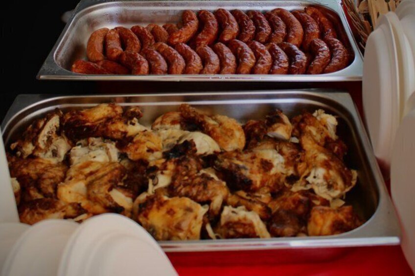 A buffet with trays of cooked sausages and chicken. 3