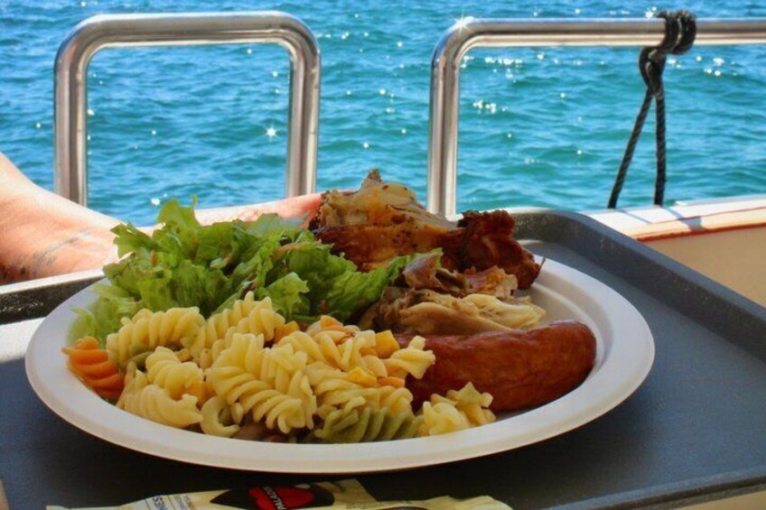 A plate of food on a boat with pasta, sausage, and greens. 2
