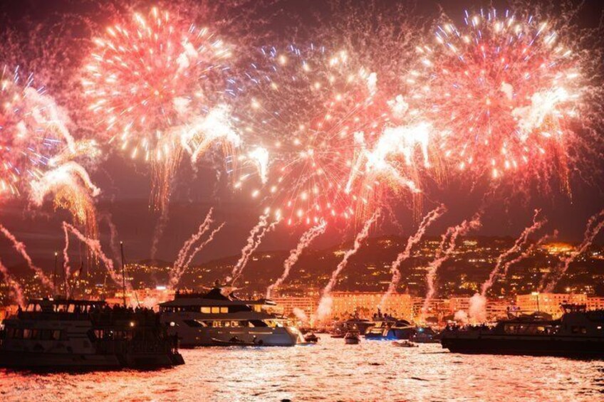 A fireworks display over a waterfront with boats and a cityscape in the background. 1