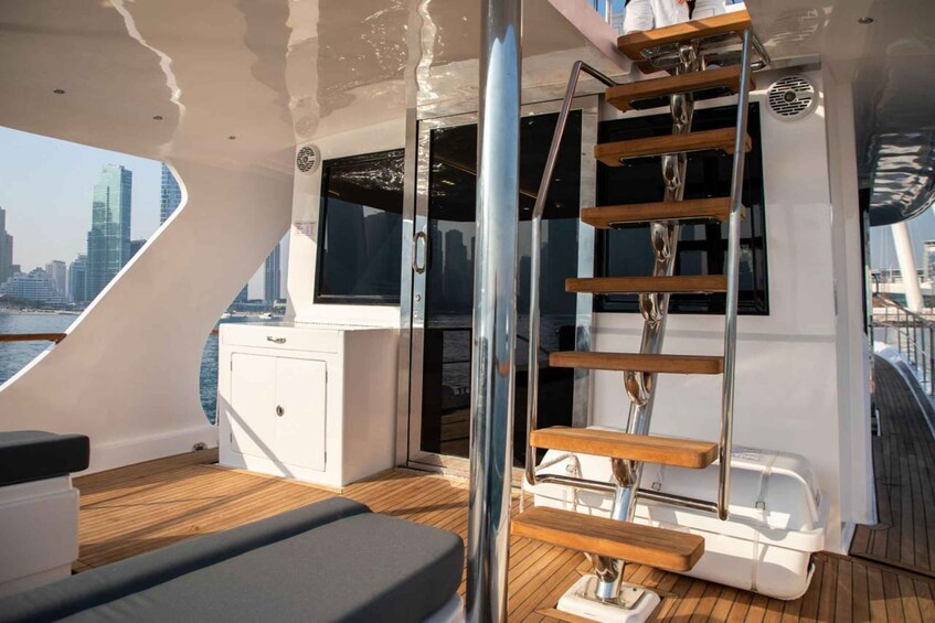 A yacht deck with a wooden staircase, cushioned seating, and a city skyline in the background. 1