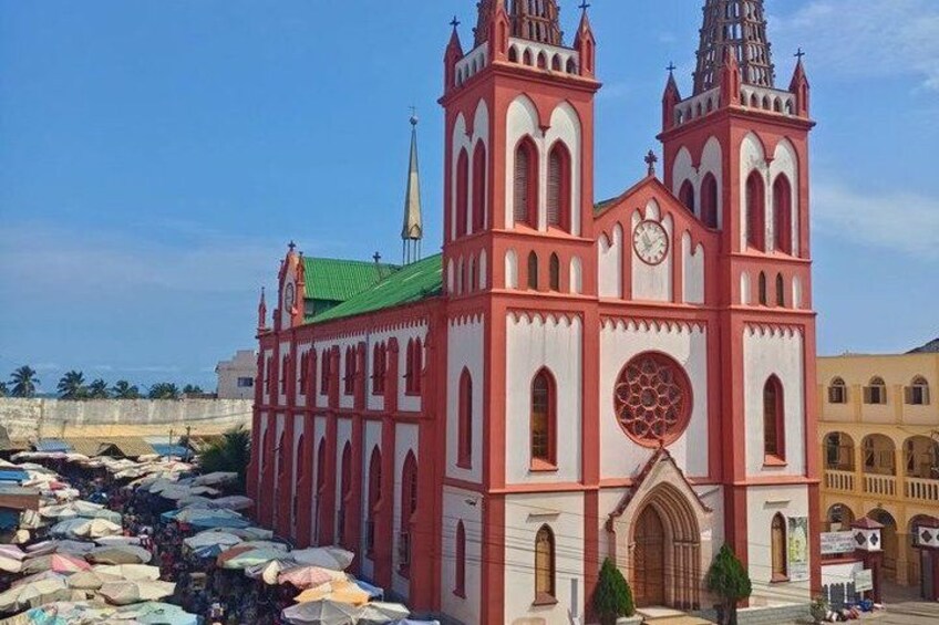 A large church with two towers and a clock, surrounded by a busy street with parked cars and a river. 2