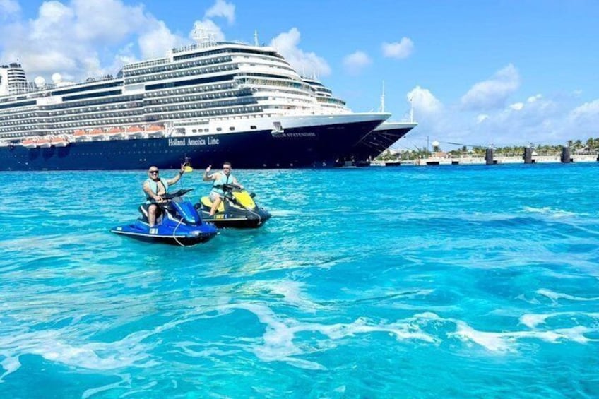A cruise ship named 'Holland America Line' with two people on jet skis in the foreground. 1