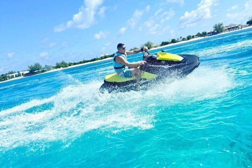 A person jet skiing on clear turquoise water with a tropical landscape in the background. 1