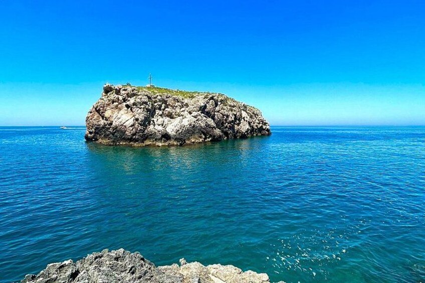 A rocky island with a cross in the center, surrounded by calm blue waters. 4
