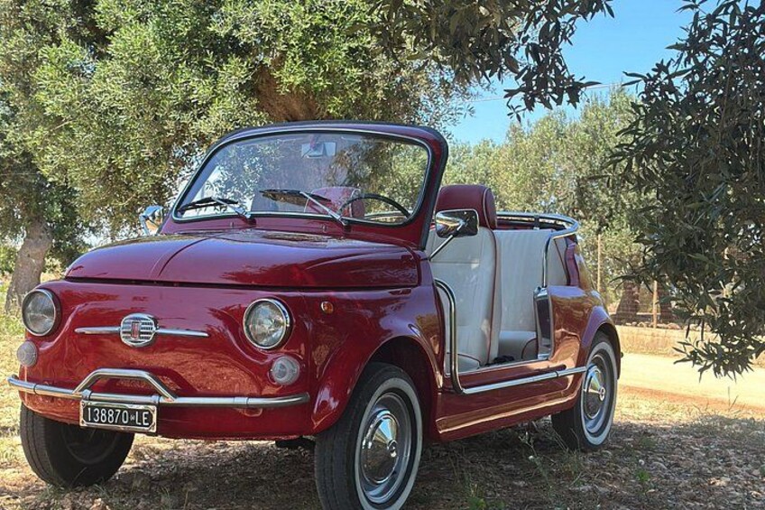 A vintage red convertible car parked under a tree. 1