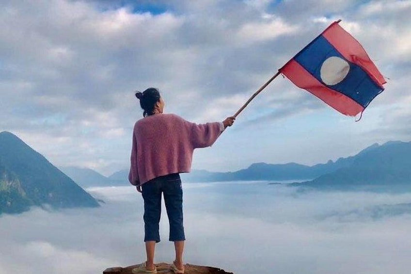 A person holding a flag on a mountain peak with clouds below. 2