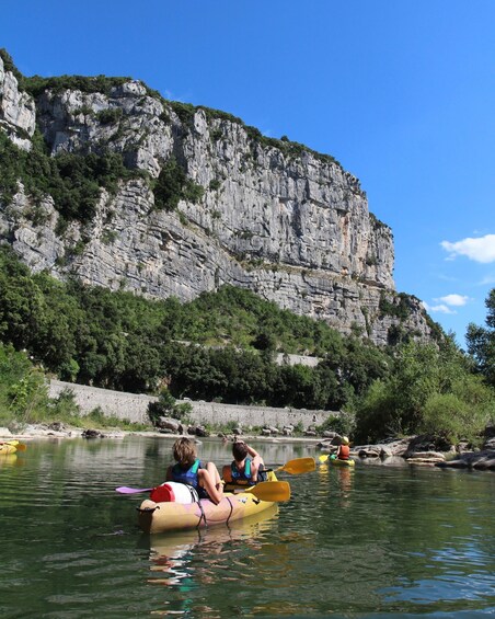 People kayaking on a river with a rocky cliff in the background. 1