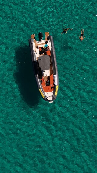 A small inflatable boat with people on board and two swimmers in the water. 2