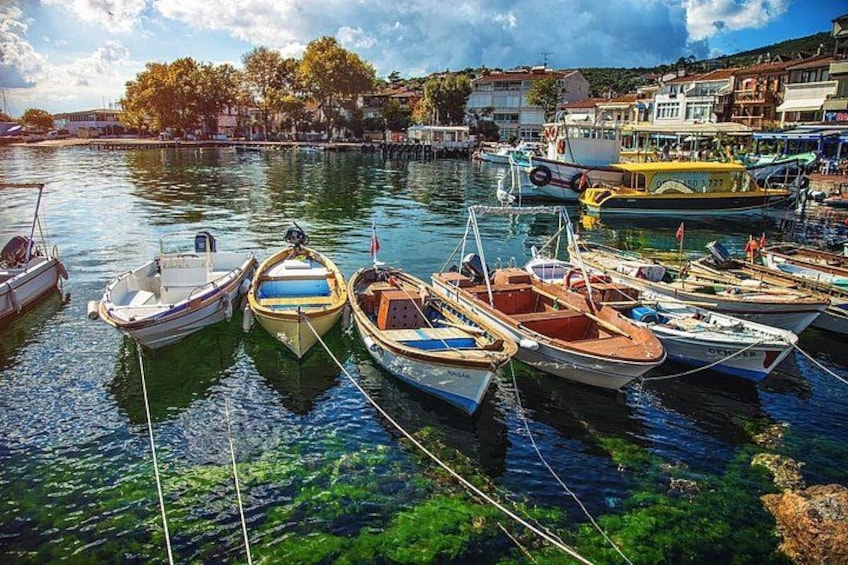 Ein Yachthafen mit mehreren kleinen Booten an den Stegen, klarem Wasser und Gebäuden im Hintergrund. 5