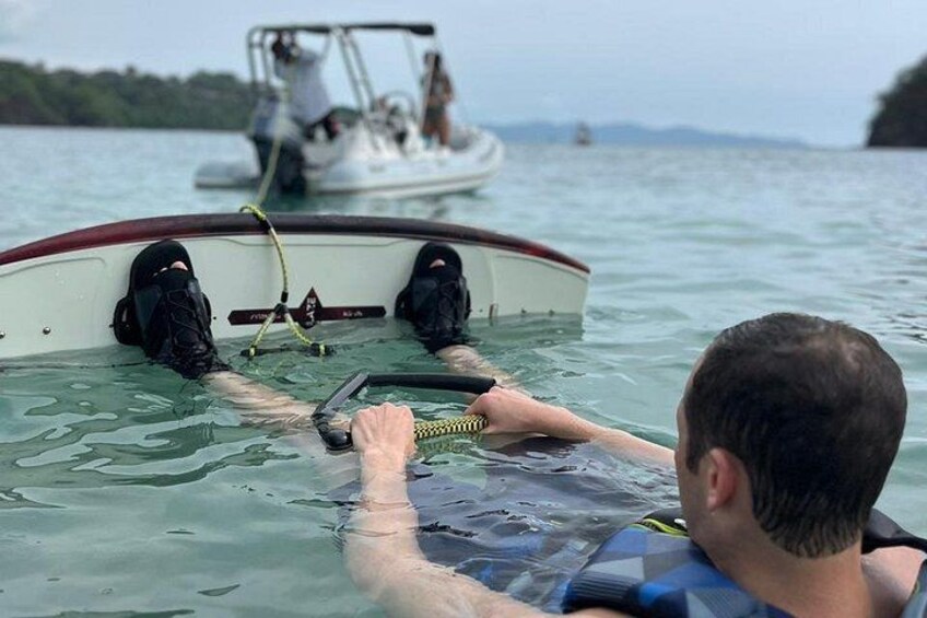 Eine Person in einem Boot mit Schwimmweste, einem Neoprenanzug und einer Hand am Seil. 4