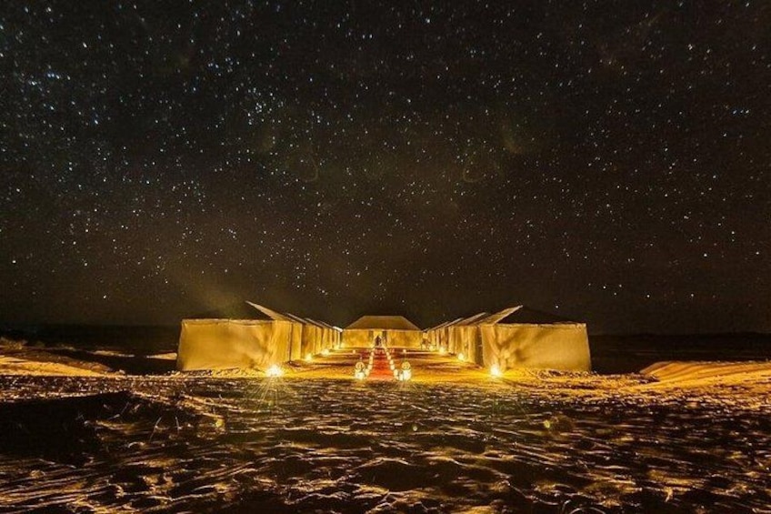 A desert landscape at night with illuminated structures and a starry sky. 5