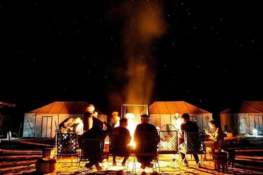 A group of people gathered around a campfire in front of tents at night. 3