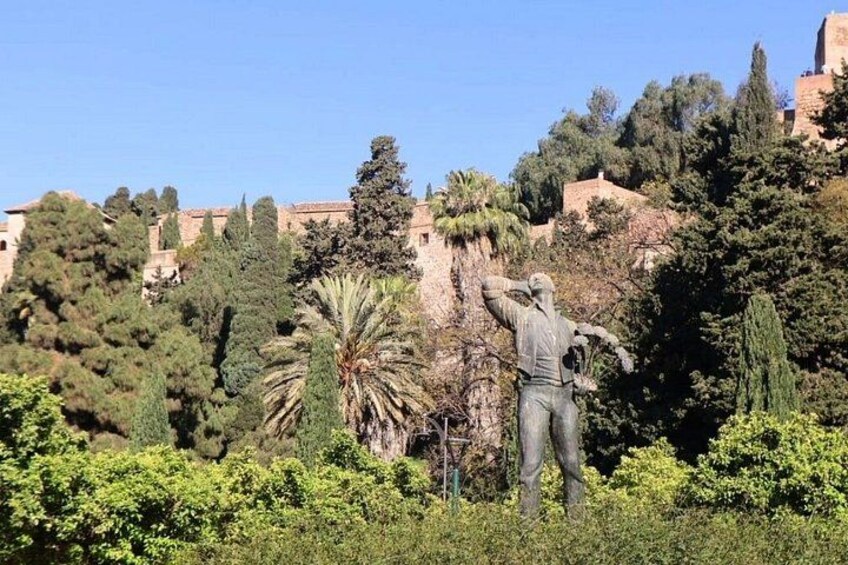 A statue of a man in a park with trees and a building in the background. 5