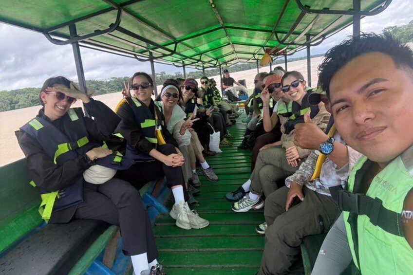 A group of people on a boat with a green canopy, wearing safety vests. 2