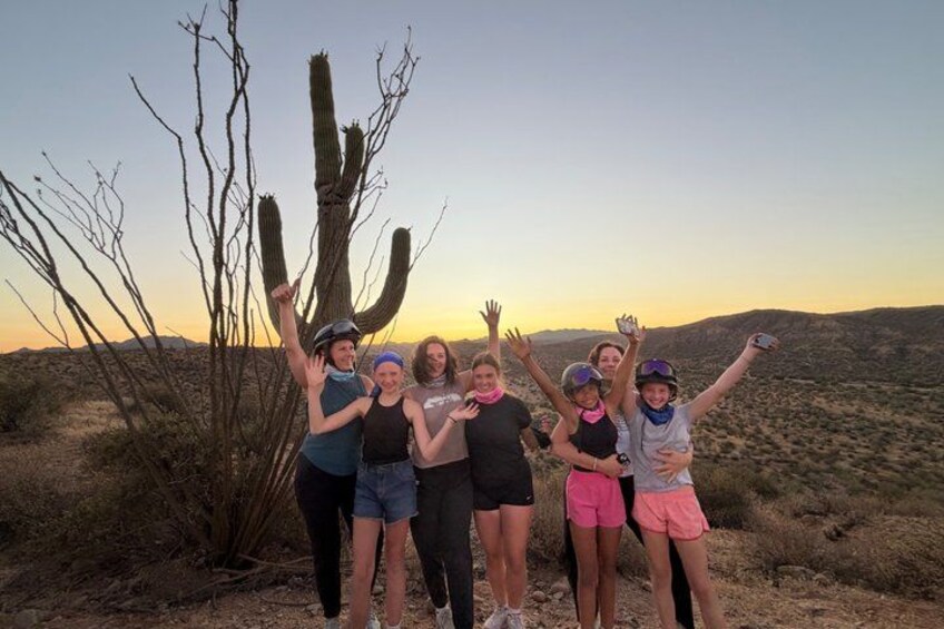 Un groupe de personnes se tient dans un désert, avec un grand cactus en arrière-plan. 5