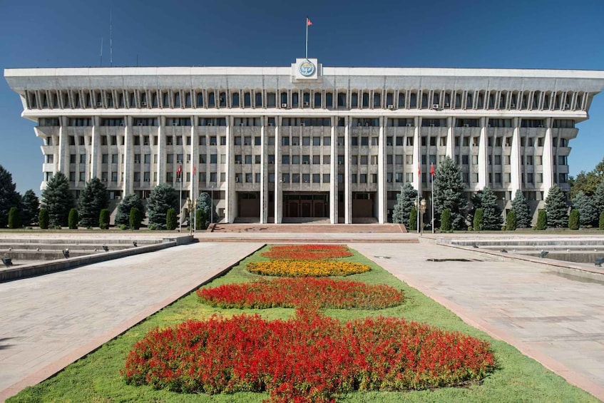 A large government building with a symmetrical facade, a central entrance, and a flagpole. 1