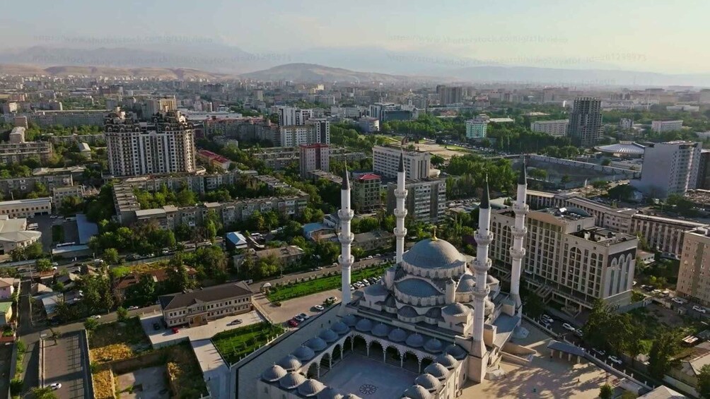 A cityscape with a prominent mosque featuring multiple minarets and domes, surrounded by modern buildings and greenery. 5
