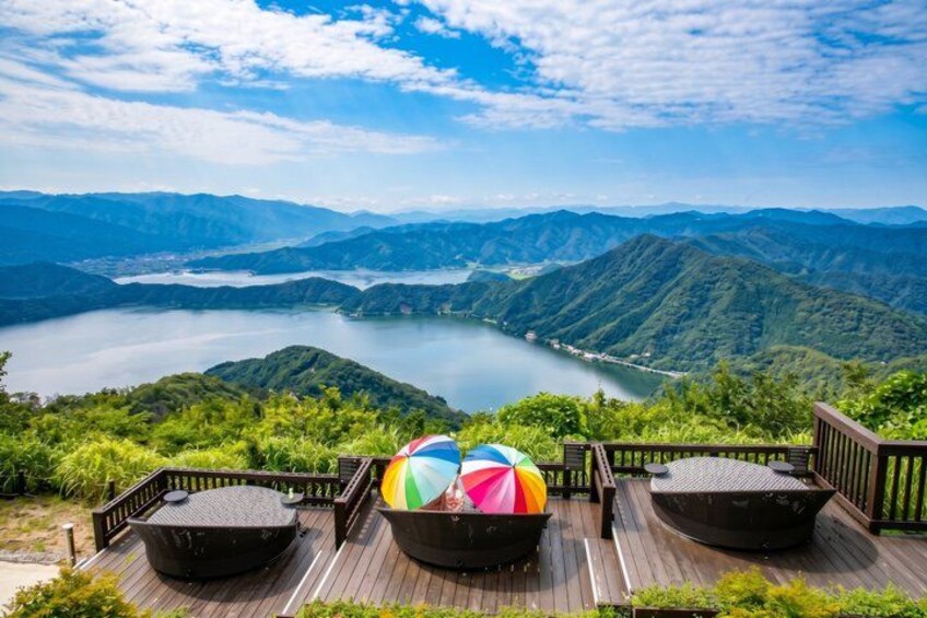 A scenic overlook with a wooden deck, a colorful umbrella, and a lake surrounded by mountains. 5