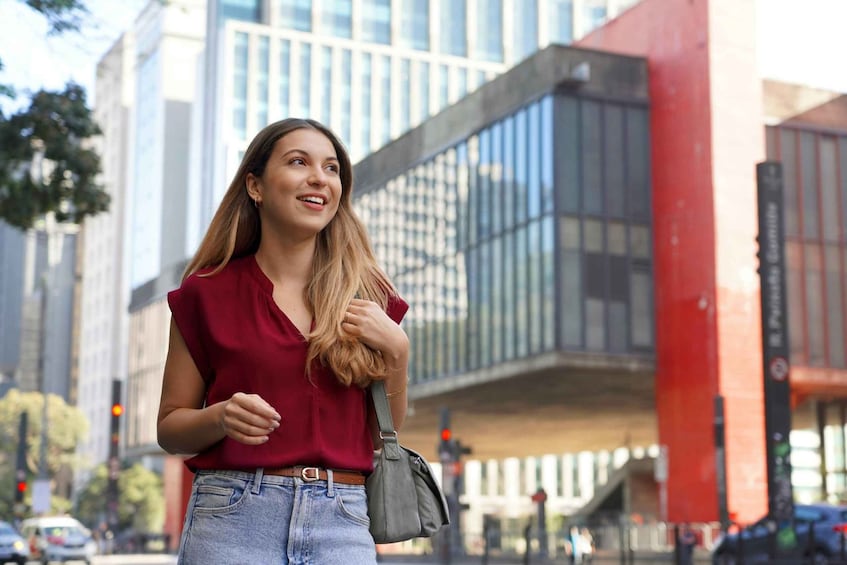 A person walking on a city street with modern buildings and a red structure in the background. 4