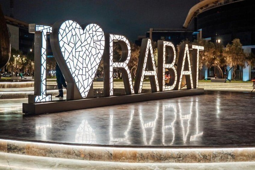 Panneau lumineux représentant le texte « I ♥ RABAT » avec un motif en forme de cœur, dont la lumière se reflète sur le sol. 5