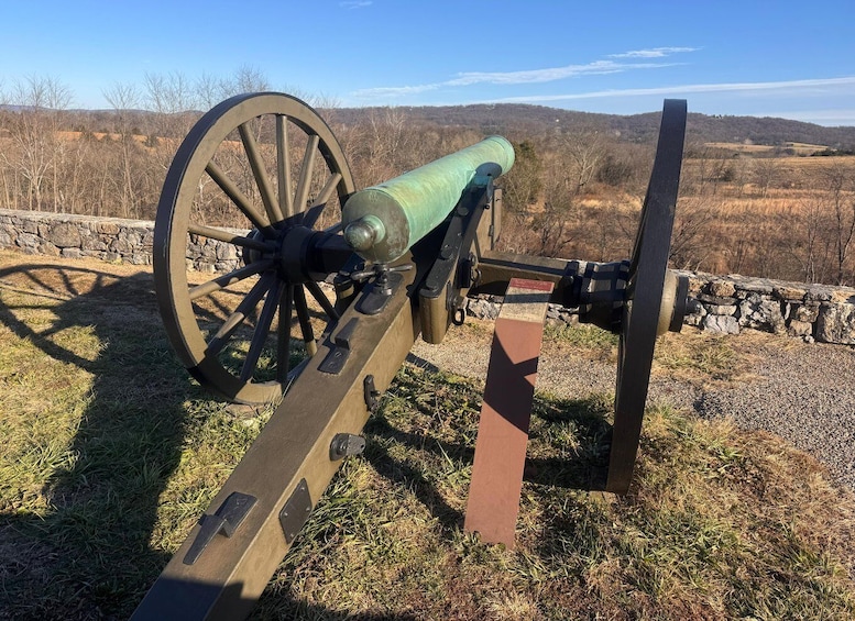 A historical cannon with a wooden carriage, set against a rural backdrop with stone walls and a clear sky. 4