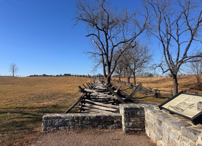A historical battlefield with a wooden fence and stone markers, surrounded by open fields and leafless trees. 5