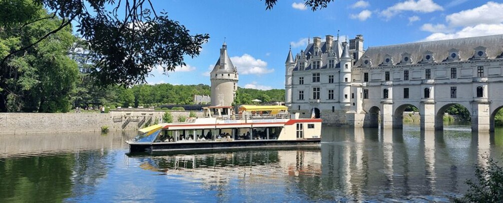 A riverboat on a calm river, a historic building with a tower, and a bridge in the background. 1