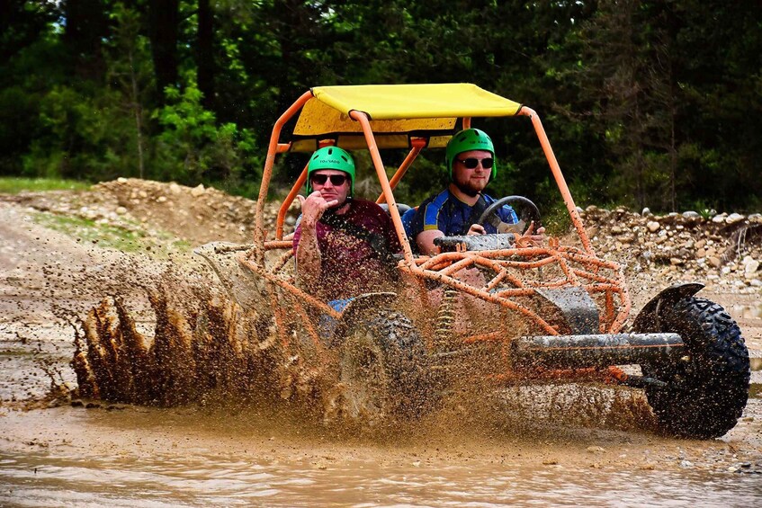 Two people in a vehicle driving through a muddy area with water splashing around. 5