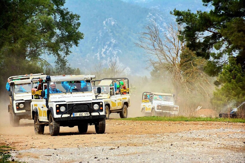 Off-road vehicles driving on a dirt road with trees and mountains in the background. 3