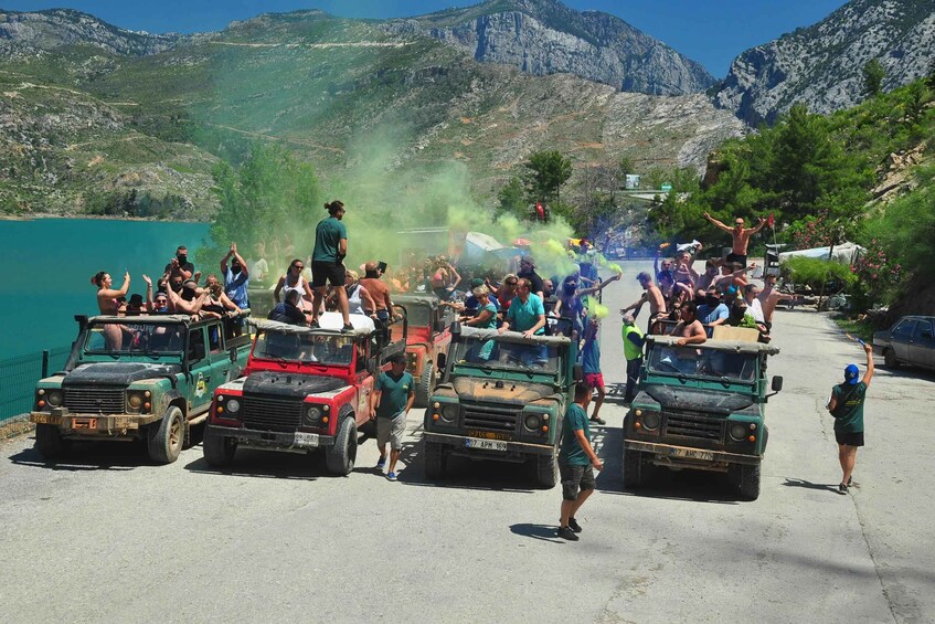 A group of people celebrating with colored smoke, surrounded by rugged mountains and parked jeeps. 2