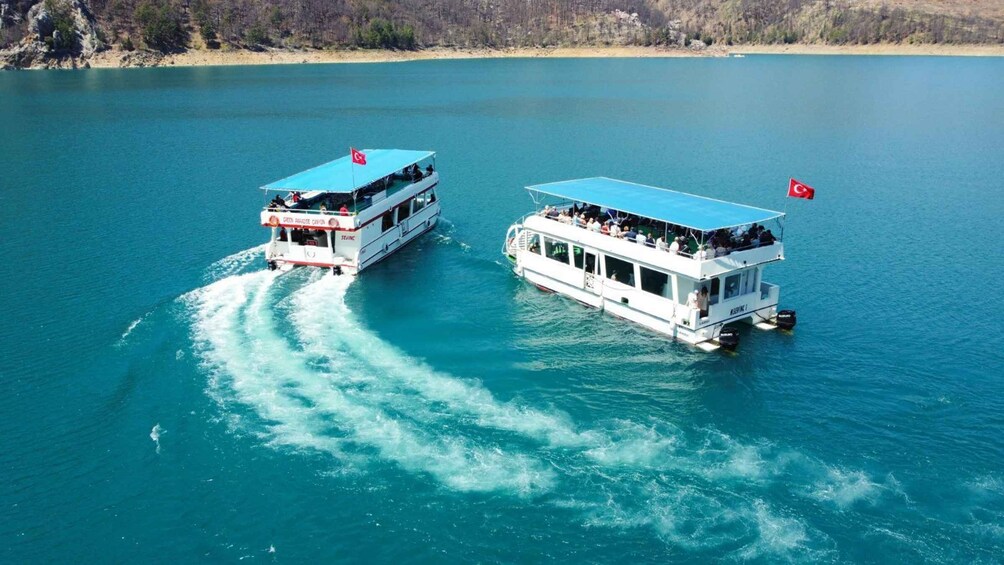 Two white tour boats with blue roofs and red flags on a turquoise lake. 4