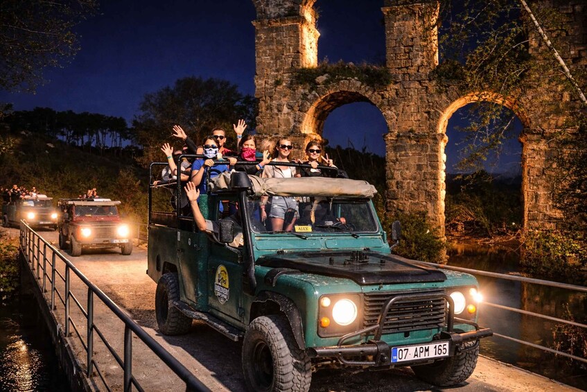 A green off-road vehicle with passengers on a bridge over a body of water, with stone arches in the background. 1