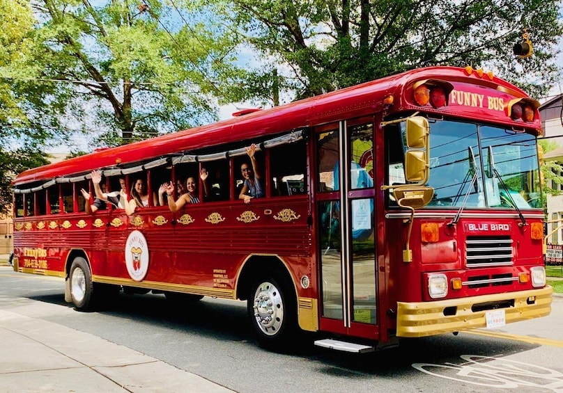 A red bus with 'Funny Bus' and 'Blue Bird' branding, decorated with gold patterns and passengers waving. 1