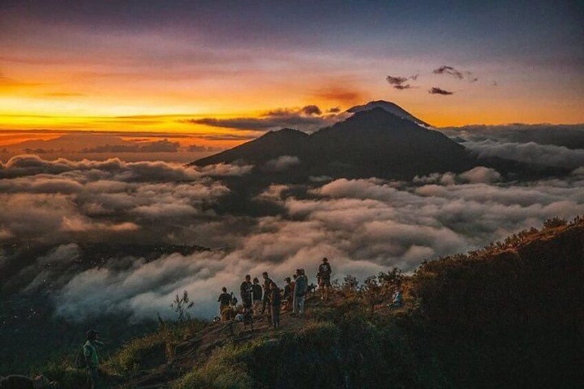 Un grupo de personas en la cresta de una montaña, con vistas a un mar de nubes y otra montaña al fondo. 3