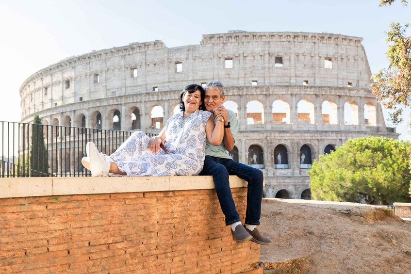 A couple sitting on a brick wall with the Colosseum in the background. 2
