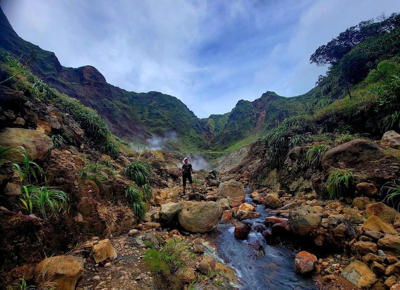 A hiker standing on a rocky stream in a mountainous valley. 2