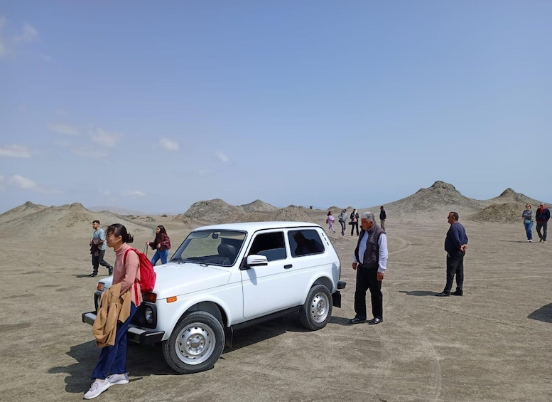 A white SUV parked in a desert with people walking around. 4