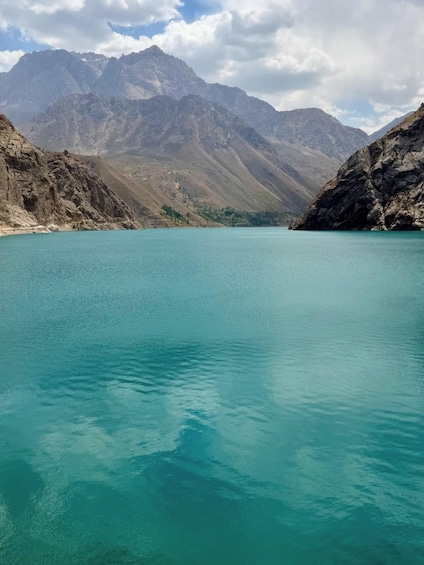 A turquoise lake surrounded by rugged mountains under a partly cloudy sky. 2