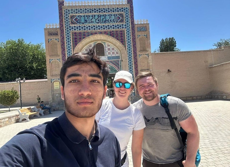 Three people in front of a historic building with intricate tile work and a large archway. 2