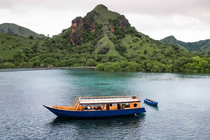 A blue boat on calm water with a forested mountain in the background. 4