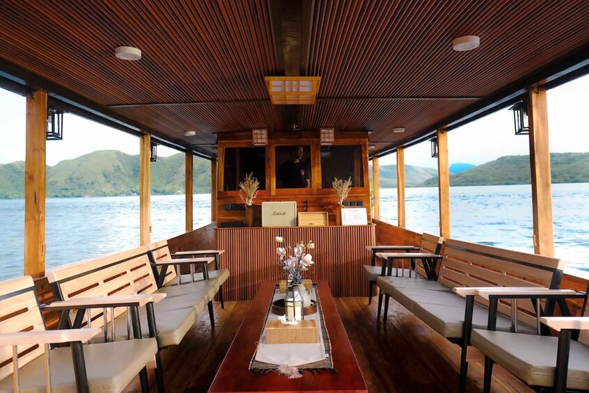 A wooden deck with benches and tables, a central table with a vase, and a view of a lake with mountains in the background. 1