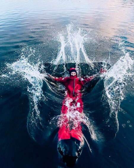 A person in a red wetsuit floating on water with arms outstretched. 1