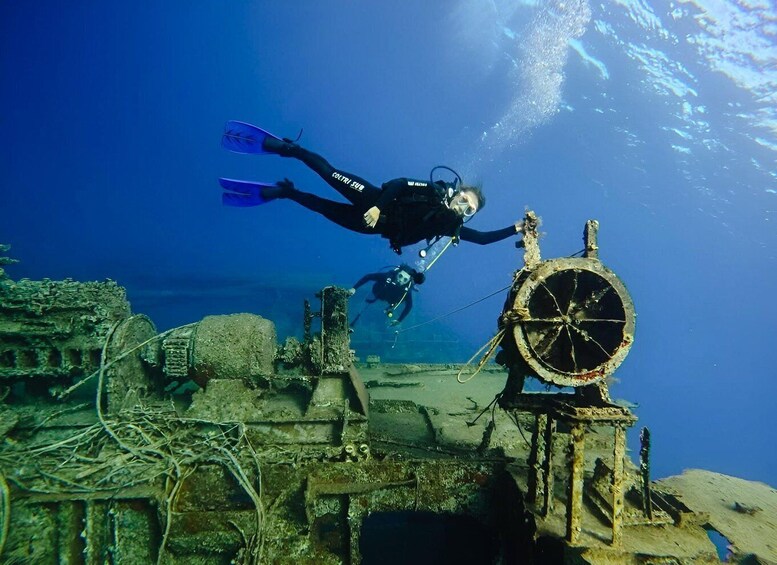 A diver exploring an underwater wreck with a large wheel structure. 1