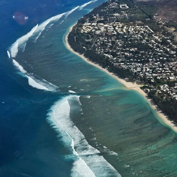 An aerial view of a coastal town with a beach, ocean waves, and dense vegetation. 2
