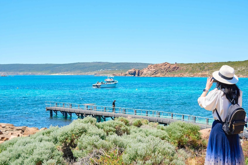 A coastal scene with a pier extending into turquoise waters, a boat, and a person taking a photo. 1