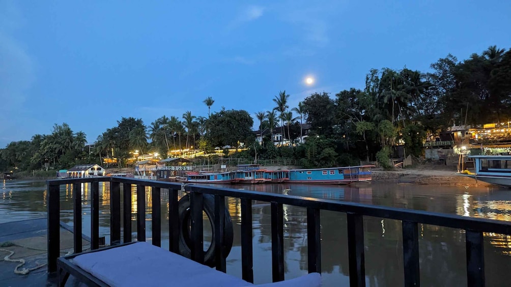 A river with boats docked, a wooden pier, and a backdrop of illuminated buildings and palm trees. 4
