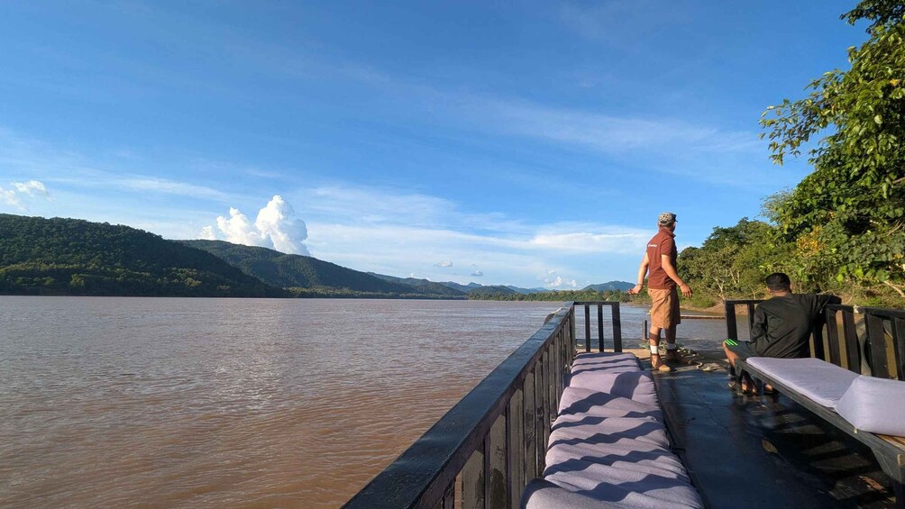 A river with a wooden dock, a person standing, and a person sitting. 5