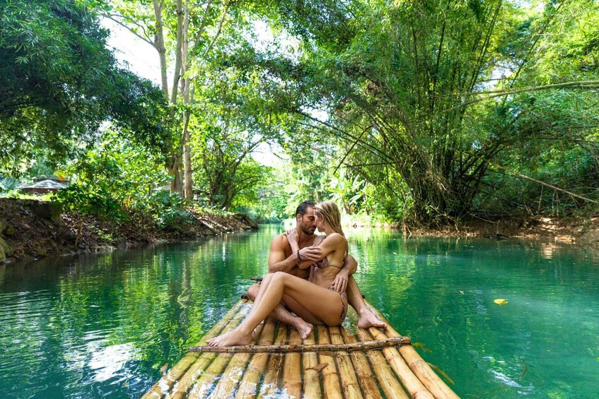 A couple sitting on a bamboo raft in a river surrounded by lush greenery. 3